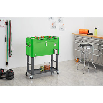 A bright green foosball table on wheels doubles as a cooler, featuring red and blue players and black handles. Below, a gray shelf holds jars of snacks, and the table has a bottle opener attached to its side.