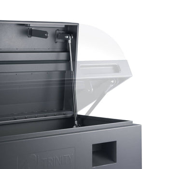A close-up shows the interior of a gray Trinity job site box with its lid partially open. A gas strut mechanism holds the lid in an elevated position, and the 