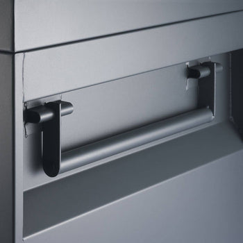 A close-up shows a horizontal, cylindrical metal handle attached to a flat, gray metallic surface with two black, L-shaped brackets. The handle appears to be part of a job site tool box.