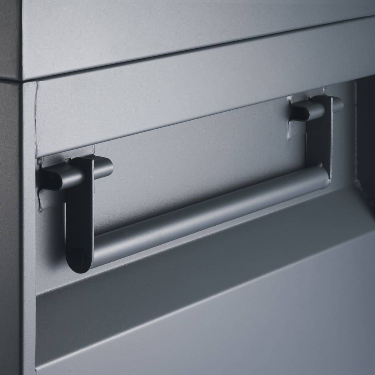 A close-up shows a horizontal, cylindrical metal handle attached to a flat, gray metallic surface with two black, L-shaped brackets. The handle appears to be part of a job site tool box.