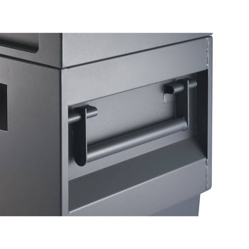 A close-up shot shows a gray metal job site box with a horizontal handle attached to its side. The handle is a simple metal bar, secured by two brackets on either end, suggesting durability and ease of transport for the heavy-duty container.
