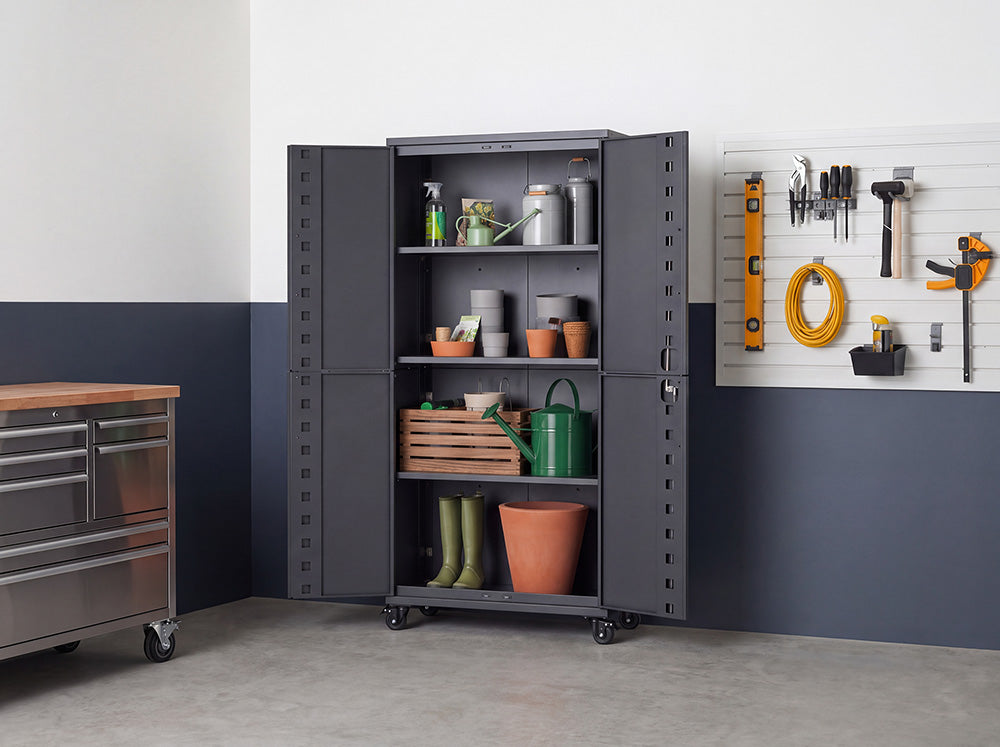 An open dark gray metal storage cabinet is neatly arranged with gardening supplies, including watering cans, terracotta pots, plant sprayers, a wooden crate, and tall boots. Set in a workshop space with a wall-mounted tool board and rolling metal workbench, the unit features wide-opening double doors and caster wheels for easy mobility.