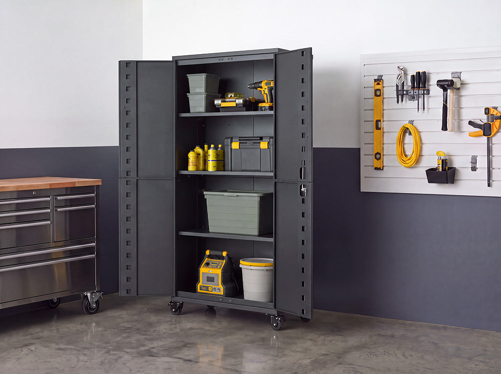 An open dark gray steel storage cabinet on wheels is filled with tools, power tool cases, fluids, and storage bins on its multi-tier shelving. Positioned in a garage workshop alongside a stainless steel tool chest and a wall slatboard with hung hand tools, its double doors swing wide open for full access.