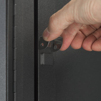A close-up view shows a person's hand operating the internal metal latch mechanism on the door edge of a dark gray steel storage cabinet. The detail highlights the functional door lock latch assembly on the powder-coated cabinet door.