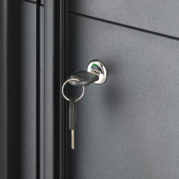 A close-up view focuses on the key-operated lock mechanism of a dark gray steel storage cabinet. A key with a key ring is inserted into the chrome cylinder lock, highlighting the cabinet's secure locking feature.