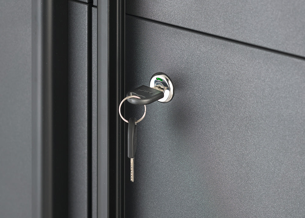 A close-up view focuses on the key-operated lock mechanism of a dark gray steel storage cabinet. A key with a key ring is inserted into the chrome cylinder lock, highlighting the cabinet's secure locking feature.