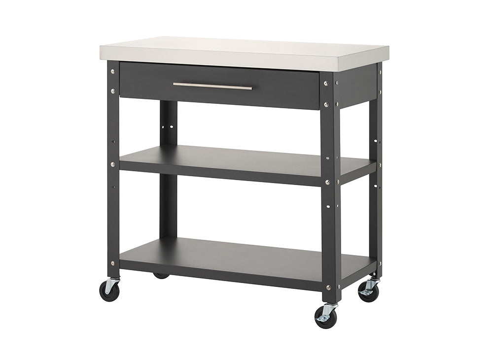 A dark gray rolling kitchen cart with a stainless steel countertop is shown completely empty against a solid white background. It features a top drawer with a silver handle, two lower open storage shelves, and four caster wheels at the base.