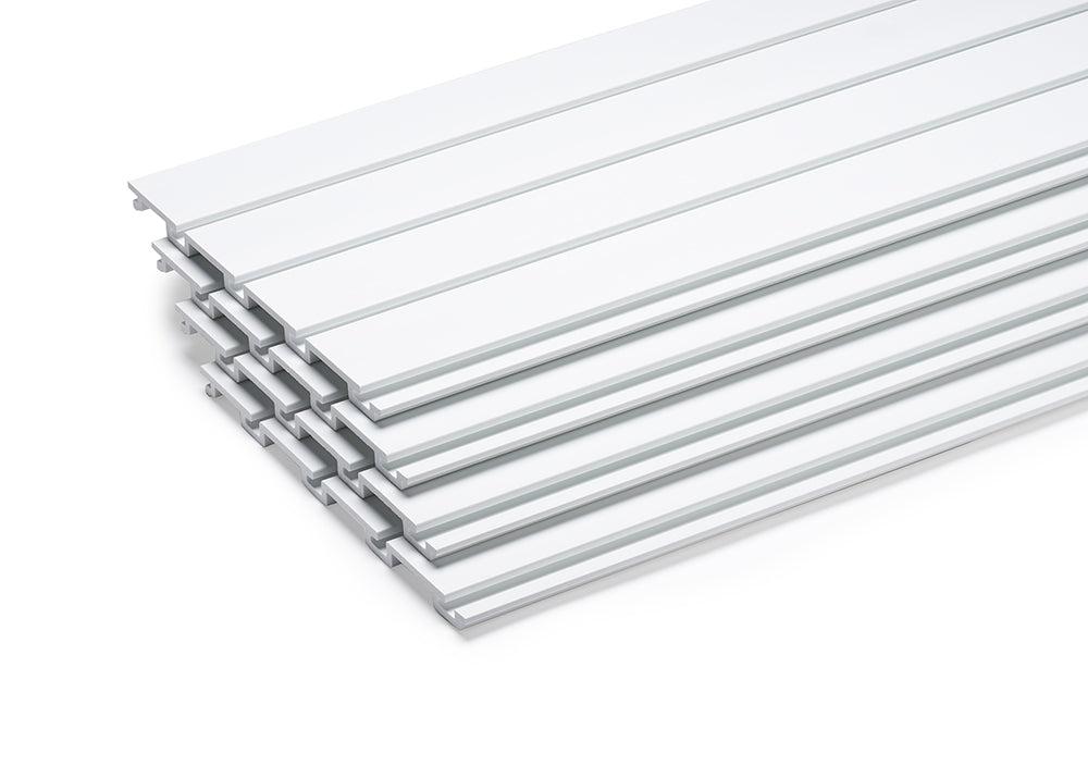 A stack of white, rectangular plastic or composite boards is shown angled on a white background. Each board has two parallel grooves running its length, suggesting they might interlock or be part of a larger slatwall system.