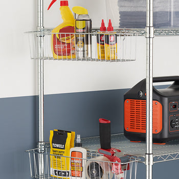 A metal shelving unit holds various garage or workshop supplies, including cleaning products, oil, and a tape dispenser. Clear wire baskets on the shelves organize the items, while a portable power station and folded towels sit nearby.