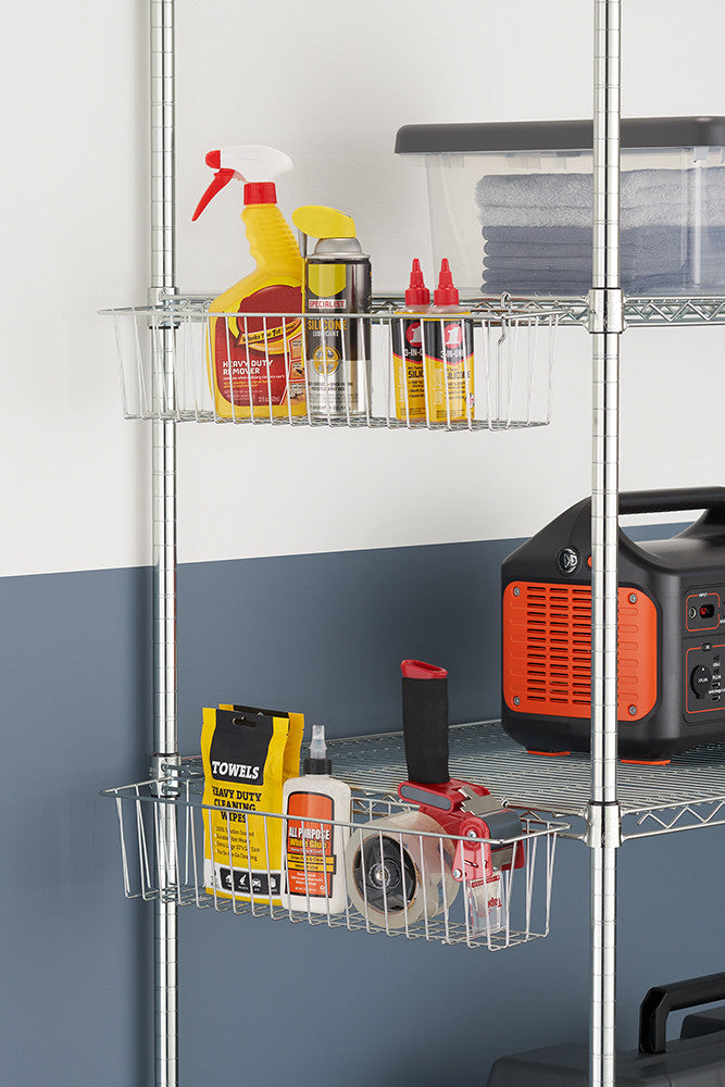 A metal shelving unit holds various garage or workshop supplies, including cleaning products, oil, and a tape dispenser. Clear wire baskets on the shelves organize the items, while a portable power station and folded towels sit nearby.