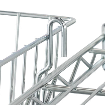 A close-up shows a shiny chrome wire basket hanging from the edge of a metal shelf. The S-shaped hook of the basket is looped over the horizontal wire of the shelf, demonstrating how the basket is attached for storage.